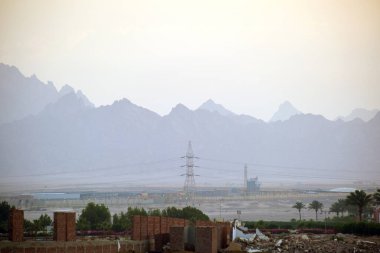 Uzak otel kompleksiyle gün batımı manzarası Mısır çölündeki karanlık dağ zirvelerine karşı.