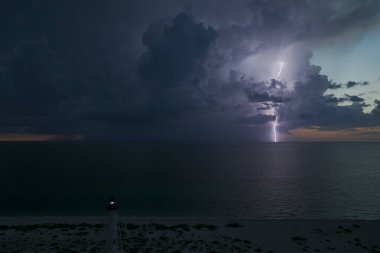 Deniz kıyısındaki uzun deniz feneri fırtınalı bir gecede ticari gemilerin seyrüsefer için yanıp sönen ışık. Okyanus üzerinde şimşekler çakan fırtına gemiler için tehlike arz ediyor..