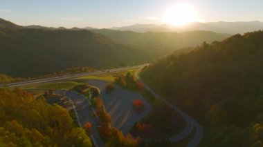 Top view of large rest area between golden fall forest near busy multilane american freeway with fast moving cars and trucks. Recreational resting place during interstate traveling thru USA mountains.