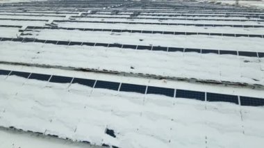 Aerial view of sustainable electrical power plant with solar photovoltaic panels covered with snow in winter for producing clean energy. Concept of low effectivity of renewable electricity in north.