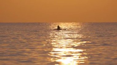 Dark silhouette of lonely fisherman rowing on his boat on sea water at sunset.