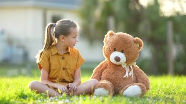 Genç ve güzel bir kız, oyuncak ayısı arkadaşını yeşil çimlerde eğlendirmeye çalışıyor. Arkadaşlık değerleri kavramı.