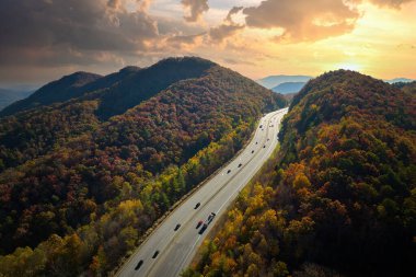 Aerial view of I-40 freeway in North Carolina leading to Asheville through Appalachian mountains in golden fall with fast moving trucks and cars. Interstate transportation concept.
