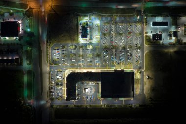 Parlak bir şekilde aydınlatılmış park yerindeki alışveriş merkezinin önünde gece park edilmiş birçok arabanın en iyi görüntüsü. Tüketim ve piyasa ekonomisi kavramı.