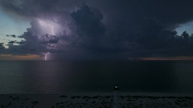 Deniz kıyısındaki uzun deniz feneri fırtınalı bir gecede ticari gemilerin seyrüsefer için yanıp sönen ışık. Okyanus üzerinde şimşekler çakan fırtına gemiler için tehlike arz ediyor..