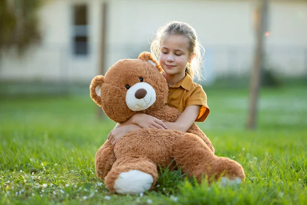 快乐的小女孩在绿草草坪上拥抱她的玩具熊朋友 友谊概念 — 图库照片
