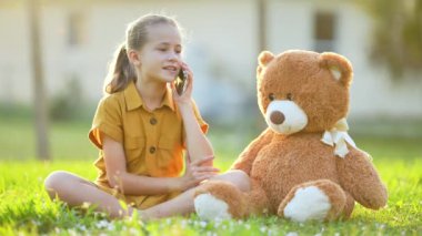 Güzel bir genç kız arkadaşıyla oyun oynayarak yeşil çimlerin üzerinde oturan açık havada telefon satıyor. Arkadaşlık değerleri kavramı.