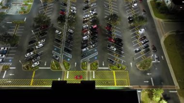 Aydınlatılmış otoparkta park yerleri ve yönler için çizgiler ve işaretler olan birçok park etmiş arabanın üzerinden görüntüyü alın. Alışveriş merkezinin önünde araçlar için yer.