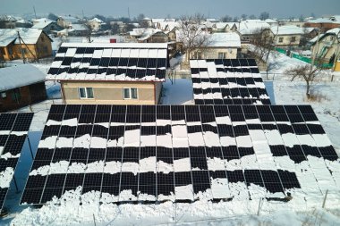 Aerial view of house roof with solar panels covered with snow melting down in winter end for producing clean energy. Concept of low effectivity of renewable electricity in northern region.