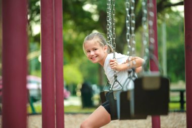 Genç, mutlu, gülümseyen küçük kız yaz tatillerinde çocuk parkında salıncaklarda eğleniyor..