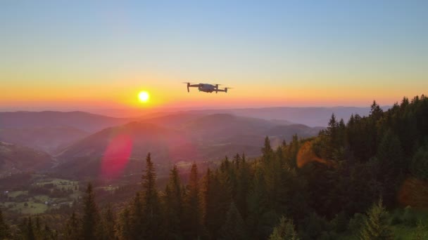 野生の山の中でカラフルな夕日の映像を撮影松の森の上を飛んで無人機の空中ビュー 明るい夕日で照らされた美しい自然景観 — ストック動画