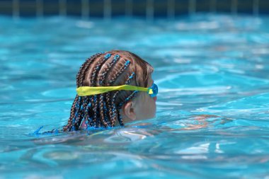 Young child girl in goggles exercises swimming in blue pool water. Summer recreation activity concept.