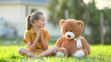 Güzel genç kız, oyuncak ayısı arkadaşıyla birlikte yeşil çimlerin üzerinde tutkuyla geziyor. Arkadaşlık değerleri kavramı.