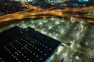 Gece vakti park yeri ve park halindeki birçok arabanın havadan görüntüsü. Araç mekanları ve yönleri için çizgileri ve işaretleri olan süpermerkez alışveriş merkezindeki karanlık otopark..
