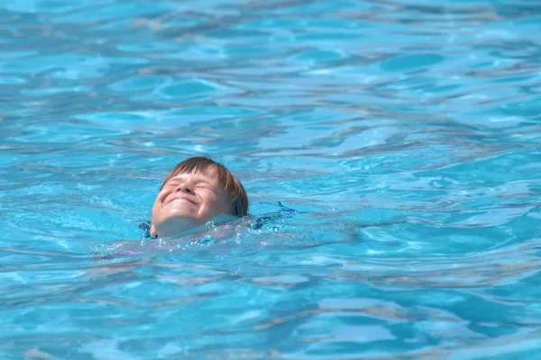 Child girl learns to swim. Funny face with closed eyes on bright blue rippled water surface.