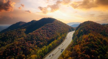 View from above of I-40 freeway route in North Carolina leading to Asheville thru Appalachian mountains with yellow fall woods and fast moving trucks and cars. Interstate transportation concept.