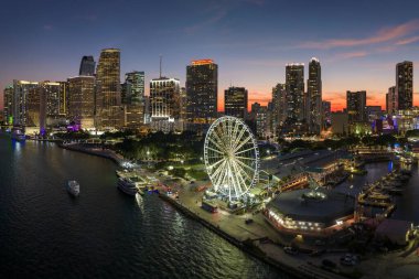 Aerial view of Skyviews Miami Observation Wheel at Bayside Marketplace with reflections in Biscayne Bay water and high illuminated skyscrapers of Brickell, citys financial center at night.