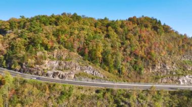 Wide highway road in North Carolina leading through Appalachian mountains with yellow fall forest and fast moving traffic. Scenic route in US national park area.