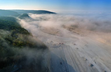 Kazı araçları ve çöp kamyonları ile inşaat endüstrisi için kireçtaşı malzemelerinin açık çukur madenciliğinin hava görüntüsü.