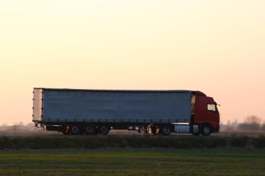 Kargo karavanı olan yarı kamyon akşam vakti otobanda mal taşır. Teslimat ulaşım ve lojistik kavramı.