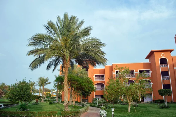 stock image Fragment of red brick resort hotel exterior with palm trees under blue summer sky.