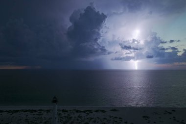 Deniz kıyısındaki uzun deniz feneri fırtınalı bir gecede ticari gemilerin seyrüsefer için yanıp sönen ışık. Okyanus üzerinde şimşekler çakan fırtına gemiler için tehlike arz ediyor..