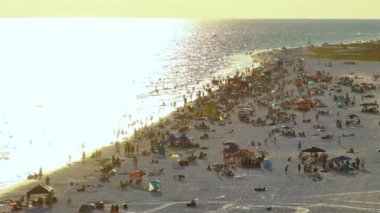 View from above of evening Siesta Key beach with white sands full of tourists in Sarasota, USA. Many people enjoing vacation time swimming in Mexica gulf water and relaxing on warm Florida sun.