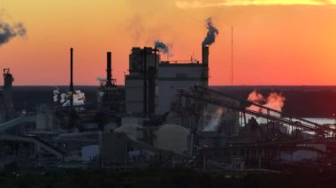 Üretim sürecinden kalma baca yığınıyla fabrika üretim sahasındaki atmosferi kirleten büyük fabrikanın havadan görünüşü. Gün batımında sanayi bölgesi.