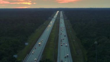 Günbatımında sürüş arabaları ve kamyonları olan geniş bir Amerikan otoyolunun yüksek açılı görüntüsü. Eyaletler arası ulaşım sistemi kavramı.