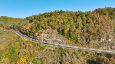View from above of national freeway route in North Carolina leading thru Appalachian mountains with yellow fall woods and fast moving trucks and cars. Interstate transportation concept.