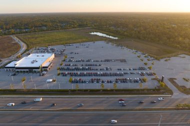 Geniş Amerikan otoyolunun yakınında satılık bir sürü yeni arabasıyla bayilik otoparkının havadan görüntüsü. ABD otomotiv sanayii kavramının geliştirilmesi.