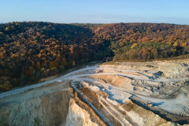 Kazı araçları ve çöp kamyonlarıyla inşaat endüstrisi için kireçtaşı malzemelerinin açık maden sahasının hava görüntüsü.