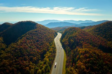 I-40 freeway road leading to Asheville in North Carolina thru Appalachian mountains with yellow fall forest and fast moving trucks and cars. Concept of high speed interstate transportation.