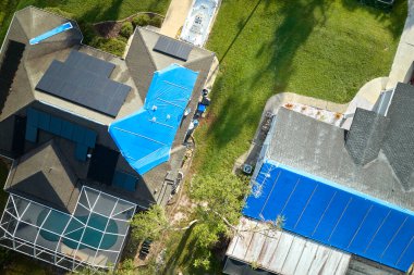 Asfalt kiremitlerin yerine konana kadar yağmur suyu sızıntılarına karşı koruyucu branda örtüleriyle kaplı çatı sızdıran evin üst görüntüsü. Florida 'daki Ian Kasırgası' nın yol açtığı çatı hasarı.