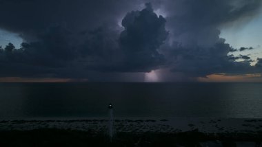 Deniz kıyısındaki uzun deniz feneri fırtınalı bir gecede ticari gemilerin seyrüsefer için yanıp sönen ışık. Okyanus üzerinde şimşekler çakan fırtına gemiler için tehlike arz ediyor..