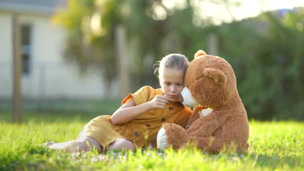 伤心寂寞的小女孩和她的玩具熊朋友一起呆在阳光灿烂的后院 青春期前的孤独 — 图库视频影像
