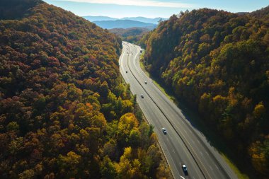 Aerial view of I-40 freeway in North Carolina leading to Asheville through Appalachian mountains in golden fall with fast moving trucks and cars. Interstate transportation concept.