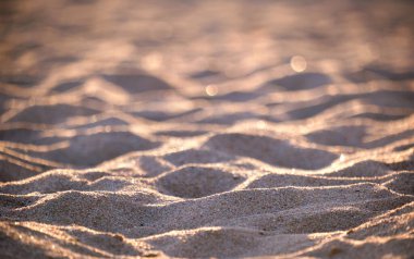 Sahil kenarını kaplayan temiz sarı kum yüzeyi akşam ışığıyla aydınlatılıyor. Seyahat ve tatil kavramı.