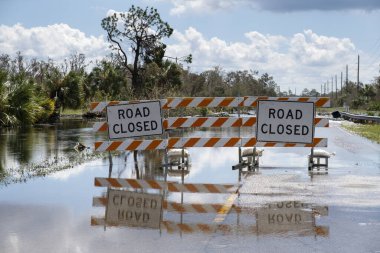 Flooded street in Florida after hurricane rainfall with road closed signs blocking driving of cars. Safety of transportation during natural disaster concept. clipart