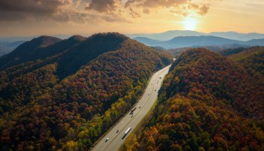 I-40 freeway road leading to Asheville in North Carolina over Appalachian mountain pass with yellow fall forest and fast moving trucks and cars. Concept of high speed interstate transportation.