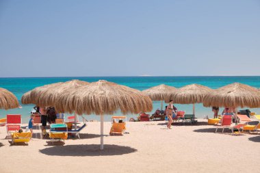 Yazın mavi renkli gökyüzüne karşı dinlenen güneşli deniz kıyılarında saman gölgesi şemsiyeleri..