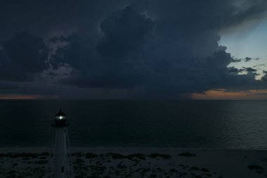 Deniz kıyısındaki uzun deniz feneri fırtınalı bir gecede ticari gemilerin seyrüsefer için yanıp sönen ışık. Okyanus üzerinde şimşekler çakan fırtına gemiler için tehlike arz ediyor..