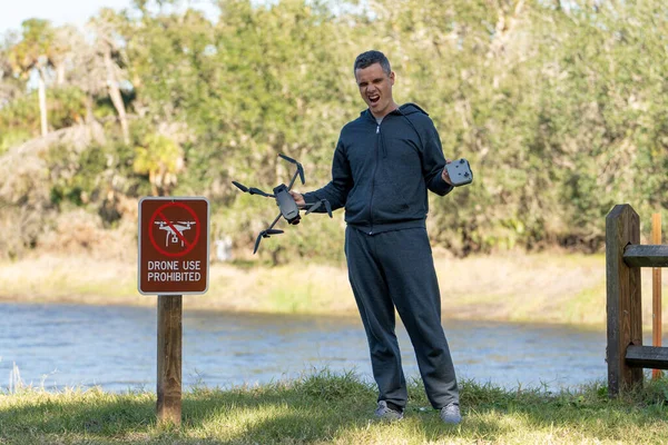 stock image Operator is disappointed because he can not fly his quadcopter in national park no drone area. Man is unable to use his UAV near restriction notice sign.