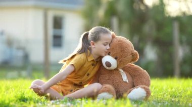 Oyuncak ayısı arkadaşıyla yeşil çimlerin üzerinde iletişim kuran sevimli bir kız çocuğu. Arkadaşlık değerleri kavramı.