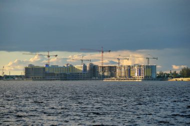 Deniz körfezi kıyısındaki inşaat alanındaki yüksek konut binalarının vinçleri ve iskelet yapısı. Rıhtımda gayrimenkul geliştirme.