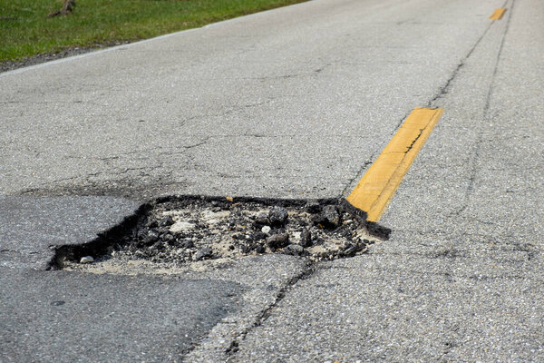 Dangerous pothole on american road surface. Ruined driveway in urgent need of repair.