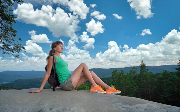Lonely woman hiker sitting alone on rocky mountain top enjoying view of nature on wilderness trail. Active lifestyle concept.
