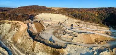 Kazı araçları ve çöp kamyonlarıyla inşaat endüstrisi için kireçtaşı malzemelerinin açık maden sahasının hava görüntüsü.
