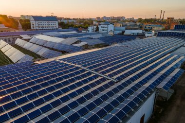 Günbatımında yeşil ekolojik elektrik üretmek için endüstriyel binanın çatısına mavi fotovoltaik paneller monte edilmiş güneş enerjisi santralinin hava görüntüsü. Sürdürülebilir enerji konsepti üretimi.