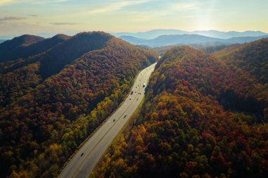 I-40 freeway road leading to Asheville in North Carolina thru Appalachian mountains with yellow fall forest and fast moving trucks and cars. Concept of high speed interstate transportation.